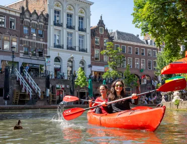 Two women paddling in a red kayak with a European town in the background