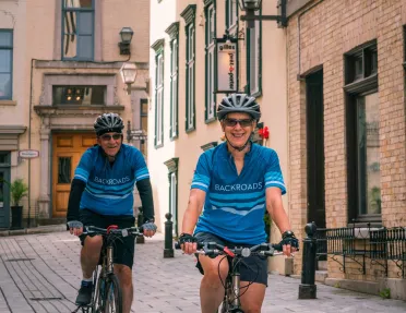 Man and woman riding their bikes along a stone alleyway in a town