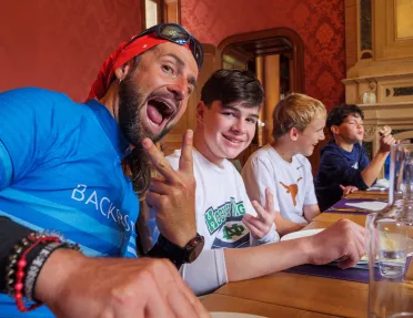 Man smiling and holding up a peace sign, with a younger teen next to him