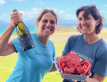 Two women smiling while holding a bottle of wine and a cooked lobster