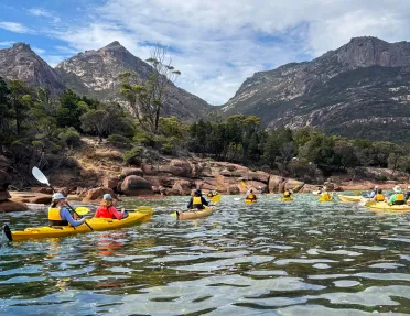 Group of people paddling in individual, yellow kayaks in a lake
