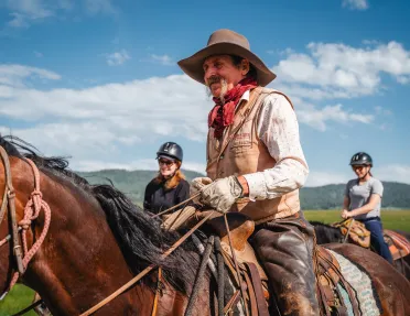 Man with cowboy gear and a long beard horseback riding