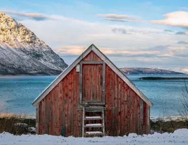 Red shed in a valley of snow with the ocean in the background