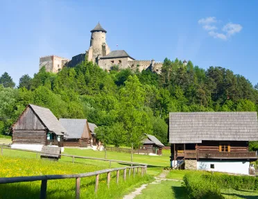 Barns on a green filed below a mountain with a castle on it