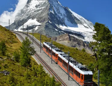 Train going down a hill, with snow-capped mountains in the distance
