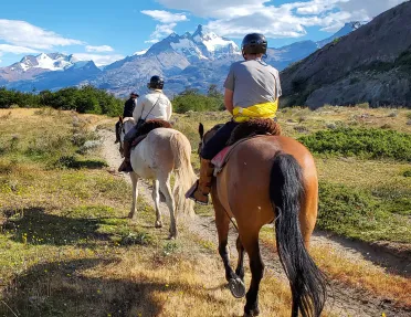 Three people horseback riding on a dirt trail in the middle of an open valley