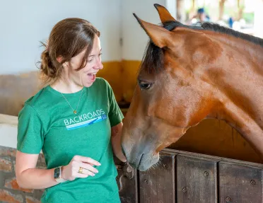 Woman in a green shirt, smiling while petting a horse
