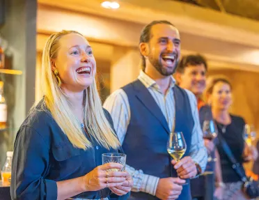 Group of men and women smiling while holding glasses of wine and spirits