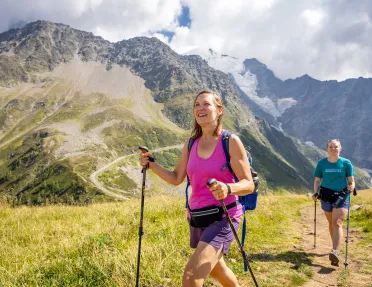Two women walking on a dirt trail, with large mountains in the background