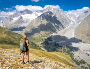 Woman wearing a backpack, looking out to a large valley of mountains and trees