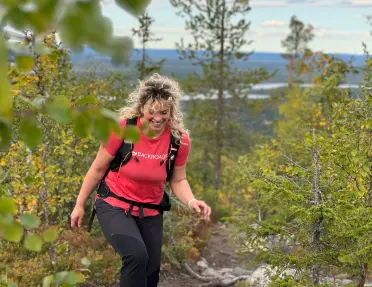 Woman in a red Backroads shirt, ascending a rocky hill surrounded by plants