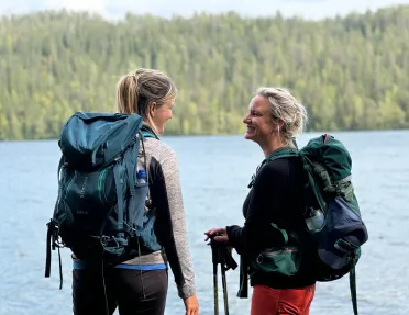 Two women smiling while standing in front of a lake