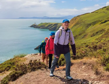Group of people walking on a dirt trail on a hill, with the ocean in the distance