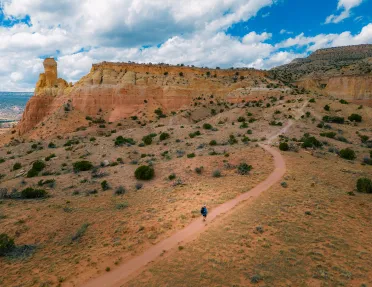 Top view of a man in blue ascending a dirt trail towards a mountain