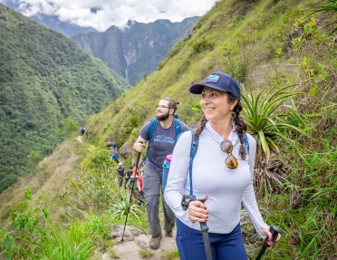 Woman and man walking on a dirt trail, smiling and looking out towards large hills
