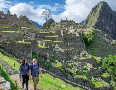 Man and woman smiling while walking on a stone path, with Machu Picchu in the background