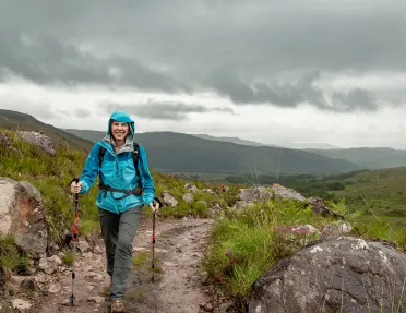 Woman wearing a blue raincoat, hiking on a dirt trail