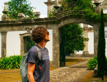 Man standing in front of a stone palace, surrounded by tall trees and bushes
