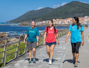 Three women walking on a stone path next to the ocean side