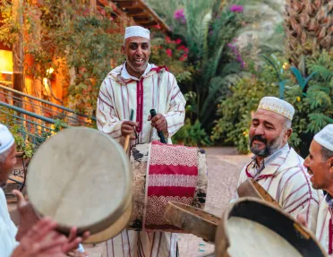 Group of men wearing white, playing bongo-like instruments