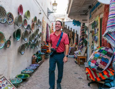 Man standing in an alleyway, surrounded by baskets and pots on the walls