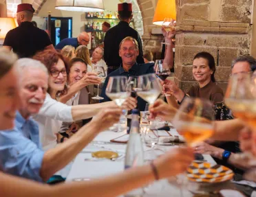 Group of people smiling while raising their glasses around a dining table