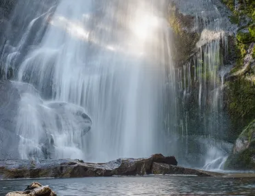 Large waterfall with a lake on the ground level, being hit by the sunlight