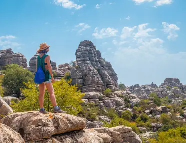 Woman standing on a large boulder, looking out towards a valley of large canyons