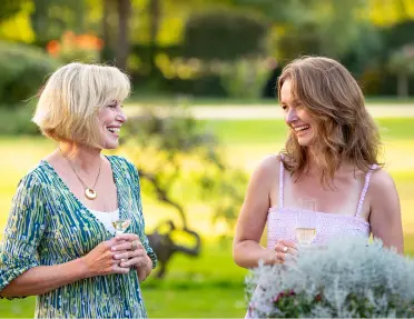 Two women looking at each other, smiling with a grass field in the background