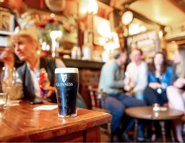 Group of people at a pub, with a full glass of Guinness beer on the tabl