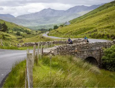 Hairpin road in the middle of a grassy valley, with two people biking on the road