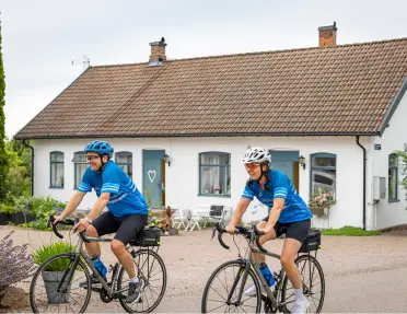 Man and woman biking on a road in front of a cottage