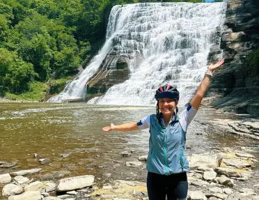 A Backroads guest poses with their hands arms raised in front of a waterfall.