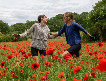 Two women joyfully running through a vibrant field of red poppies in Provence, France.