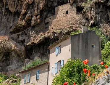 Traditional Provencal houses nestled into a rocky cliffside, with vibrant red poppies in the foreground—part of the scenic route from Provence to the French Riviera.