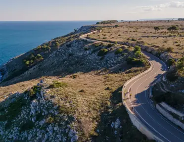 Cyclists ride along scenic, winding coastal road along the rugged cliffs.