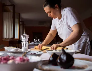 A person wearing a white short-sleeve collared shirt and a white apron, rolls out dough in the dining area of Ristorante da Luisa.