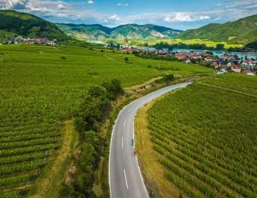 Long road leading to a small lake-side town, with two bikers on the road