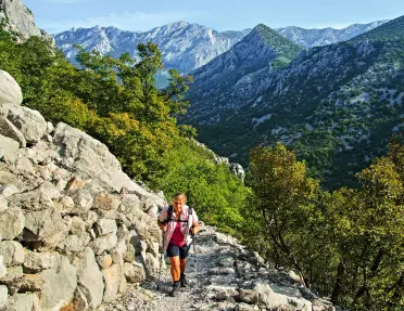 Woman ascending a rocky trail with large mountains in the background
