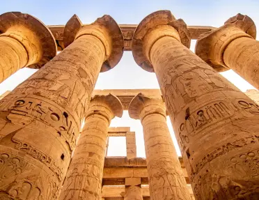 The Great Hypostyle Hall within the Karnak Temple complex in Luxor, Egypt featuring massive columns with hieroglyphics, and ancient symbols. 