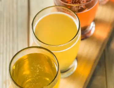 A cider flight served in a set of four small glasses on a wooden paddle.