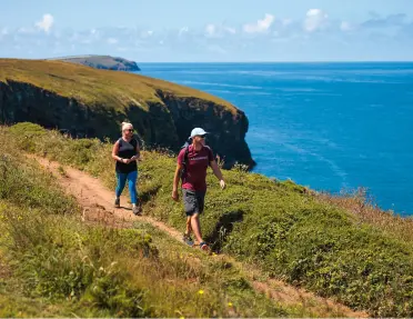 Two people walking along a dirt trail with the ocean in the background
