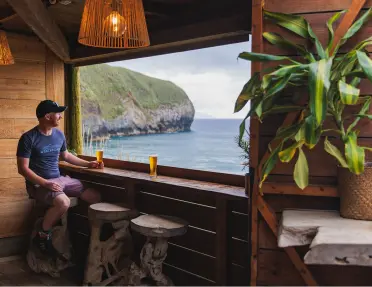 Man sitting on a stool, holding a beer and looking out towards the ocean