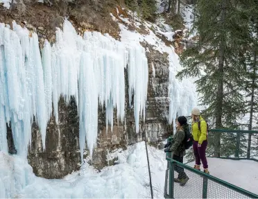 Two women standing on a balcony looking at large, frozen waterfalls