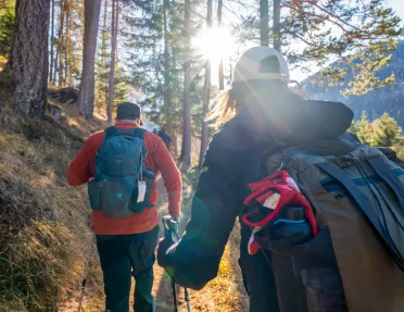 Man and woman hiking on a trail with tall trees and sunlight in the distance
