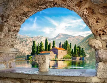 Stone arch with a view to a beige building surrounded by a lake