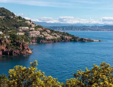 View of a bay in the French Riviera. A scenic town flows down from the hillside as blue water flows into the bay.