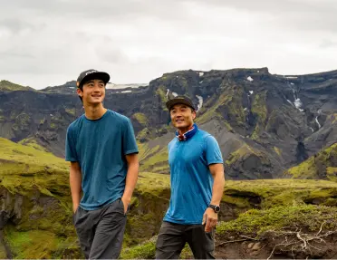 Two men smiling while walking in a valley with large mountains in the background