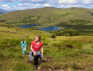 Two women ascending a grassy hill, with a lake in the distance