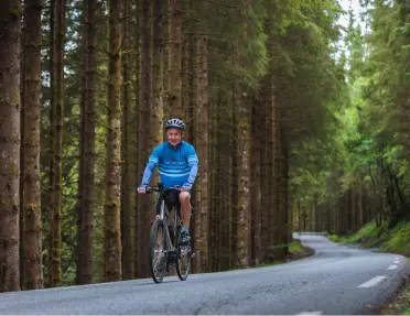 Man biking on an empty road in the middle of a forest